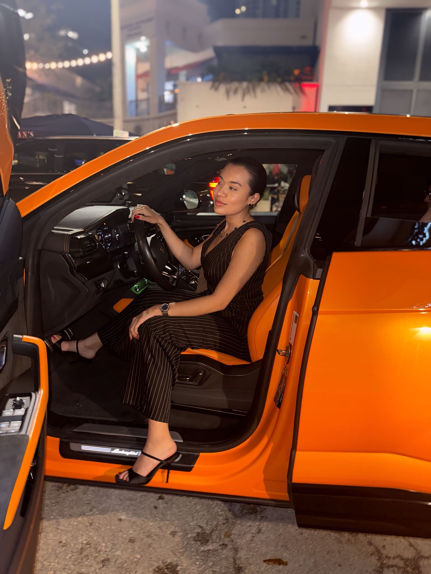Alicia seated in an orange Lamborghini