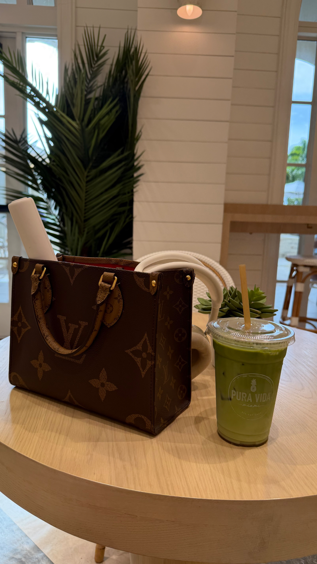 A Louis Vuitton bag and green drink on a café table
