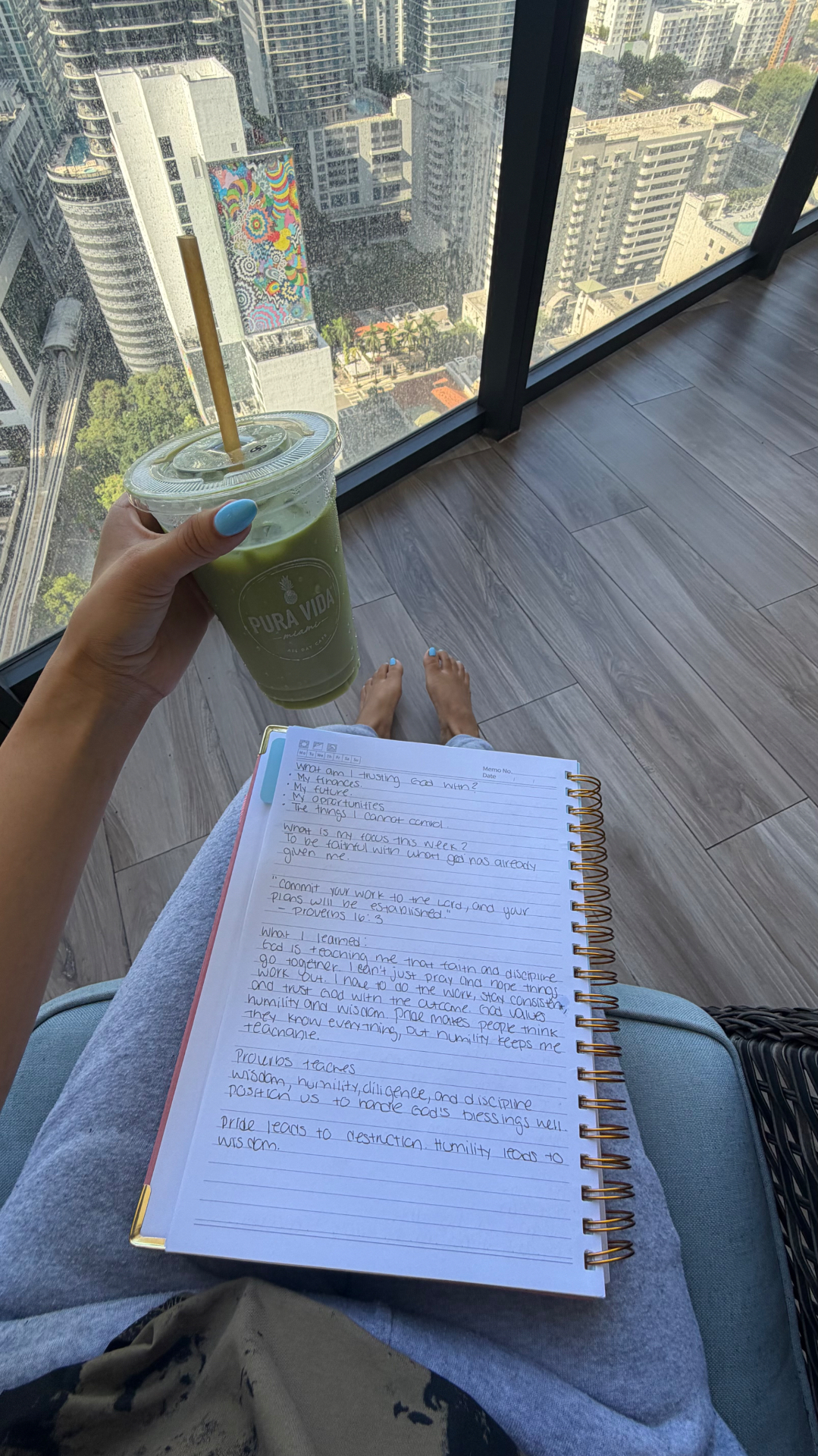 Alicia journaling with a green drink beside a high-rise window